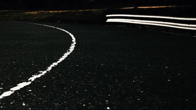 A winding road stretches into the darkness, illuminated only by soft white lines. The atmosphere is quiet and serene, perfect for late night journeys or contemplative drives.