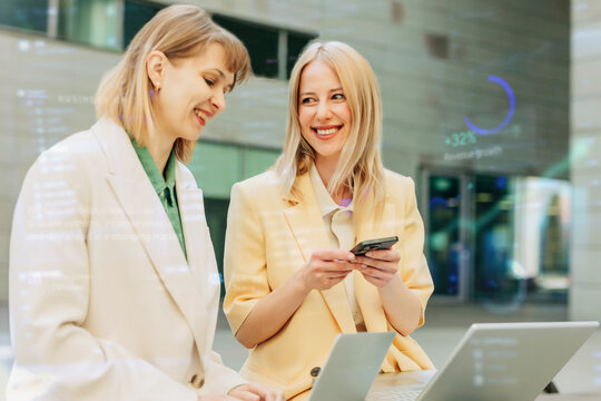 Smiling businesswomen collaborate on laptop outdoors