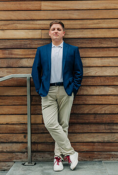 A smiling businessman leans against a wooden office building wall