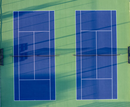 Aerial view of two tennis courts with blue and green surfaces and long shadows in Woodhaven, Michigan, United States.