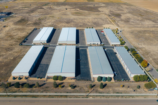 Aerial view of a self storage facility with multiple long metal buildings, paved driveways, and surrounding dry landscape in Dacono, Colorado, United States.