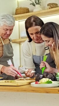 Three people in aprons decorate pastries together in a bright home kitchen, using piping bags and focusing on details for a homemade dessert.