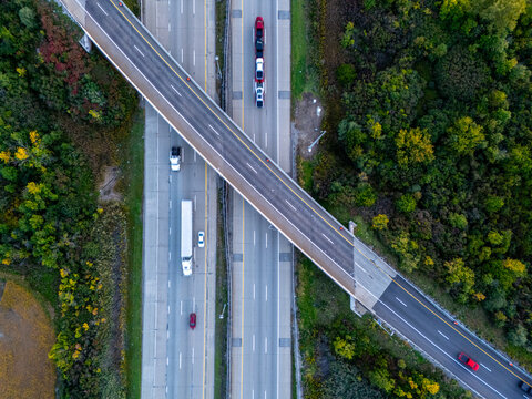 Aerial view of the I-75 Freeway intersection with vehicles driving on the asphalt lanes surrounded by dense autumn foliage in Monroe, Michigan, United States.
