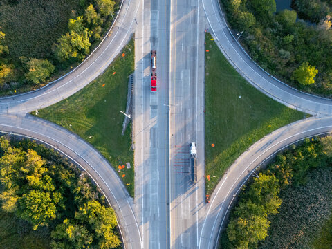 Aerial view of I-75 Freeway interchange with trucks driving on the highway surrounded by green trees and grassy medians in Monroe, Michigan, United States.