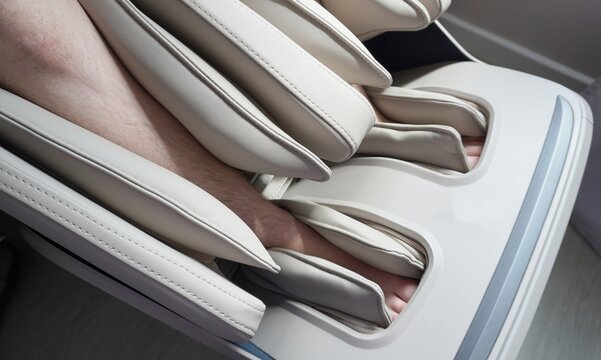 Foot massage machine in use. Close-up of lower legs and feet inserted into a beige leg and foot massager with multiple padded air bags, home wellness device on the floor,indoor setting,no face visible
