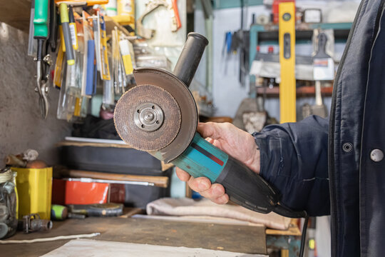 A technician holds an electric angle grinder in a messy workshop, representing professional metalworking, construction maintenance, and industrial equipment repair tasks in a garage