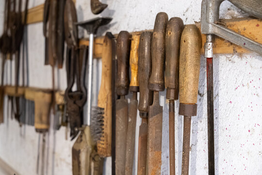 Vintage metal files with wooden handles hang on a cluttered workshop wall, representing manual labor, craftsmanship, tradition, renovation projects, and industrial heritage maintenance