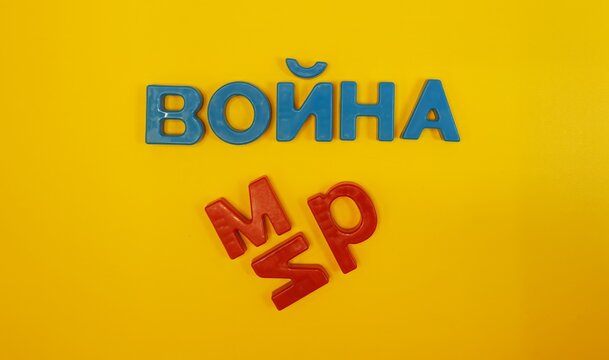 Yellow background with magnetic Cyrillic letters. The blue word "War" and the scattered red letters "peace". Cyrillic script, studio shooting.