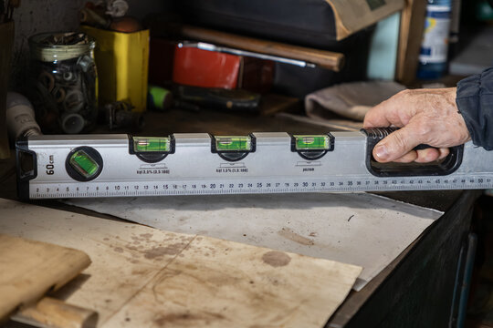 A hand holding a professional spirit level on a workbench, showing precision measurement tools during carpentry or construction work in a workshop to ensure flat surface accuracy