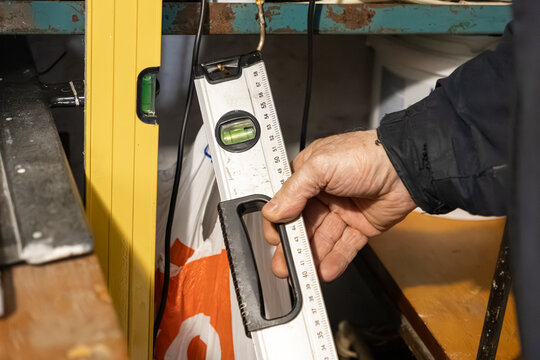 A construction worker holds a metal spirit level in a workshop, checking alignment with a precision measuring tool to ensure accuracy during a professional renovation building project