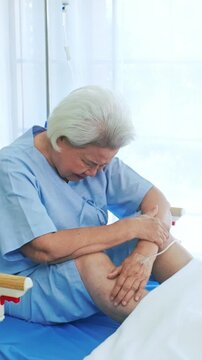 Elderly woman patient sits on a hospital bed holding her knee in discomfort, with an IV line nearby, showing senior healthcare, medical care, joint injury, treatment and recovery.