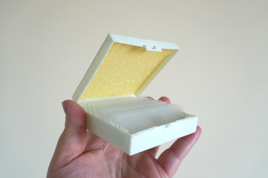 The hand holds a box with microscope slides, an open lid with foam, a neutral background, a close-up.