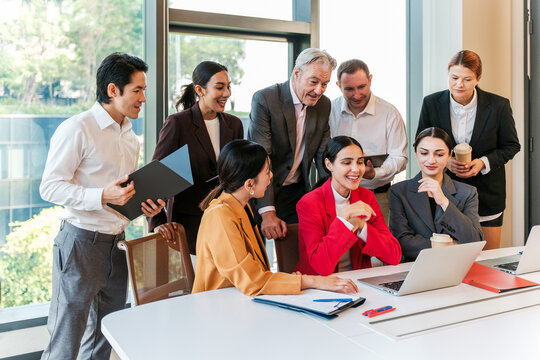 Diverse business team gathers around a laptop in a bright modern office, sharing ideas through teamwork, collaboration, leadership, planning, communication and strategy.