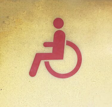 Red wheelchair accessibility symbol on textured wall. Universal disabled access sign, indicates barrier-free facilities, inclusive infrastructure and public services.