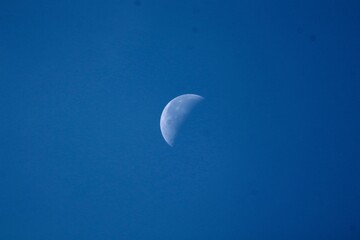 Waxing crescent moon against a deep blue daytime sky © Viktor