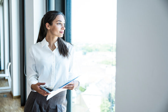 Businesswoman holds a notebook and smartphone by the office window