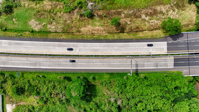 Aerial view of the Soreang-Pasir Koja Toll Road with cars driving on the asphalt lanes, surrounded by lush green trees and vegetation in Bandung, West Java, Indonesia.