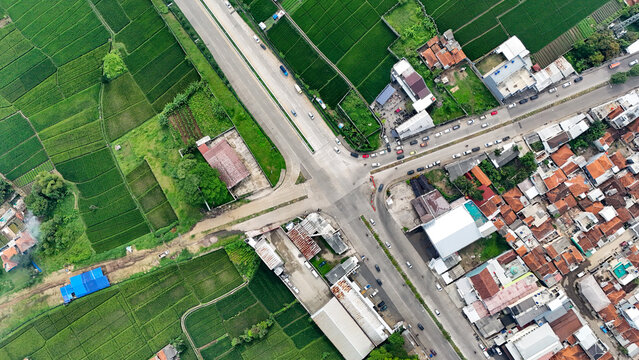 Aerial view of the Soreang intersection in Bandung, featuring a junction between roads, surrounding lush green rice fields, and dense residential buildings in Bandung, West Java, Indonesia.