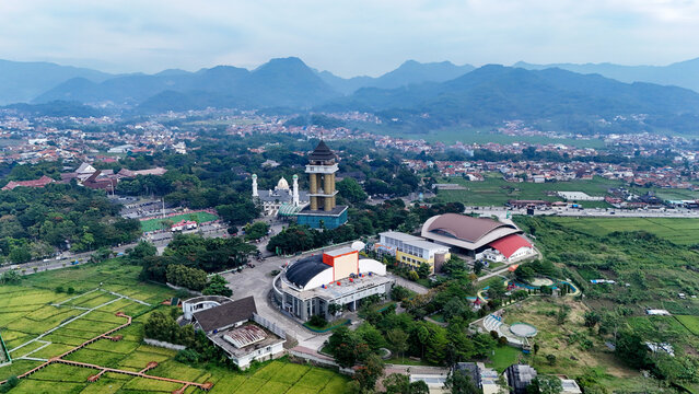 Aerial view of the Al-Fathu Mosque and surrounding Soreang area, featuring lush green rice fields, modern buildings, and distant mountains in Bandung, West Java, Indonesia.