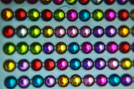 A close-up photograph showcasing neat rows of vibrant, multi-colored sparkling plastic rhinestones and gemstone stickers arranged on a sheet. Perfect for crafts, DIY projects, fashion design.