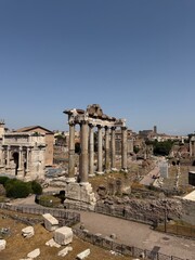 Panoramic view of the Roman Forum in Rome, Italy, featuring the Temple of Saturn, Arch of Septimius Severus and ancient ruins under a clear blue sky. Historic architecture and cultural heritage. © Yana Perelotova
