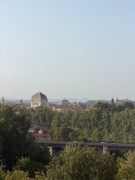 Scenic city view of Rome from Parco Savello, with historic domes, green treetops and urban architecture under a clear sky.