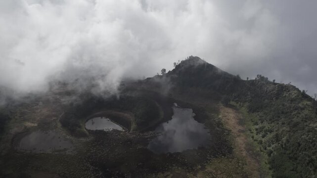Aerial View of Dramatic Volcanic Crater Lake Surrounded by Thick Mist and Clouds in a Moody Highland Landscape of Kawah Bulan Sabit, Banyuwangi, East Java, Indonesia.