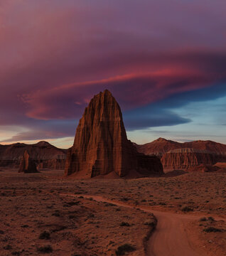 Aerial view of the Temple of the Sun and Moon monoliths rising from the desert floor under a dramatic purple and orange sunset sky in Hanksville, Utah, United States.