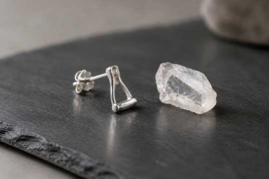 Sterling silver stapes bone earring and quartz crystal on dark slate, jewelry presentation.