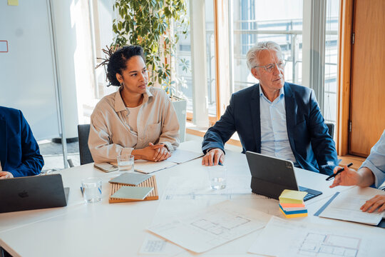 A businessman and a businesswoman discuss blueprints at the office