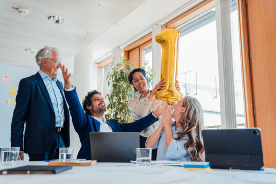 Business team celebrating first anniversary with golden balloon in office