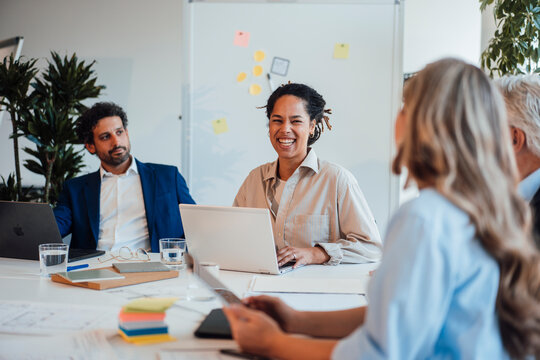 A smiling businesswoman leads an office meeting with her team