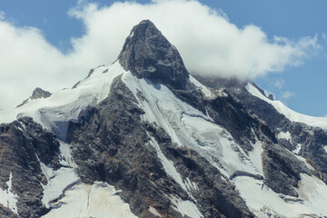 Pyramidal mountain peak rises above broad snow and ice fields in a close landscape photograph with gray rock and bright clouds for high altitude exploration and travel themes © angel_nt
