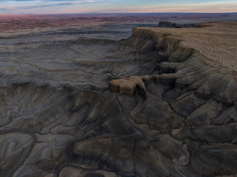 Aerial view of the rugged badlands and eroded sandstone formations under the soft light of golden hour in Hanksville, Utah, United States.
