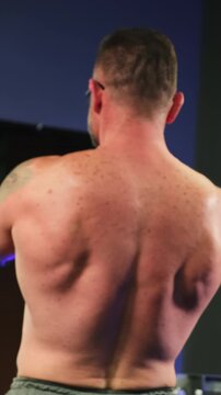 Powerful athlete lifts heavy dumbbells in front of large mirror. Strong bodybuilder strengthens arms and shoulders. Vertical video