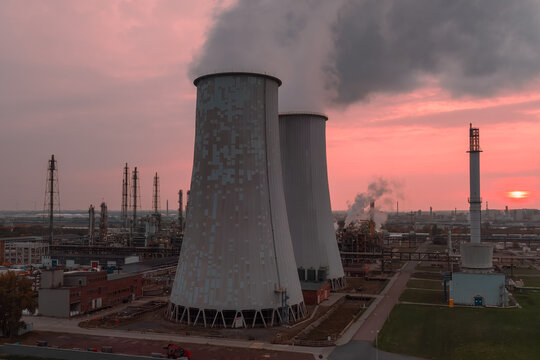 Aerial view of cooling towers at the Leuna chemical complex with steam rising against a vibrant sunset sky in Leuna, Saxony-Anhalt, Germany.