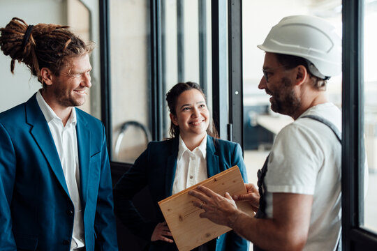 Smiling business people discuss wood with a carpenter indoors