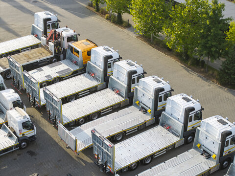Aerial view of a row of flatbed trucks parked in a lot with trees in the background in Krakow, Lesser Poland Voivode, Poland.