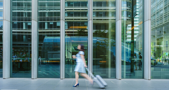 Blurred businesswoman walks past a glass building with luggage