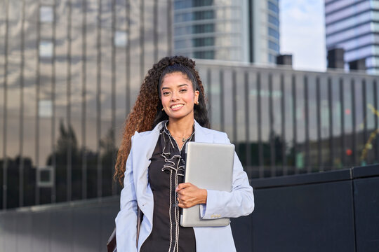Smiling businesswoman holds a laptop outdoors in the city