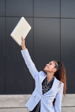 Smiling businesswoman lifts laptop outdoors to celebrate success