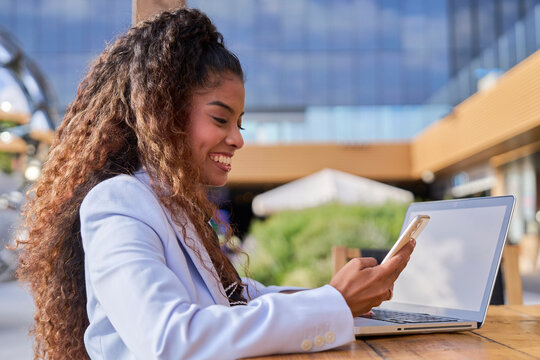 Smiling businesswoman uses smartphone and laptop outdoors