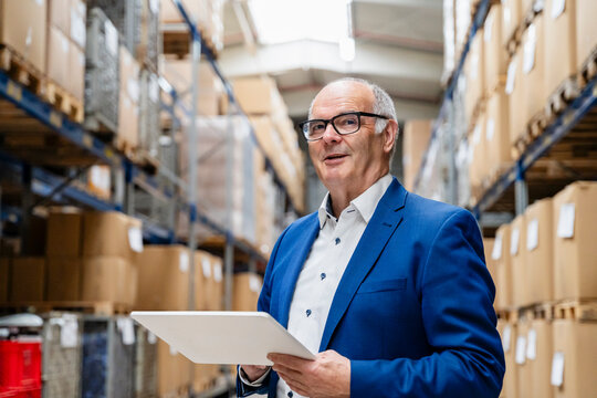Businessman holds tablet in warehouse for logistics planning