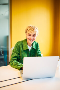 A smiling businesswoman works on a laptop in an office