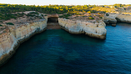 Naklejka na ściany i meble Sand beach among rocks on evening sunset. Ursa Beach near Arcos Naturais da Praia da Marinha at Atlantic Ocean coast in Portugal. Summer landscape. 