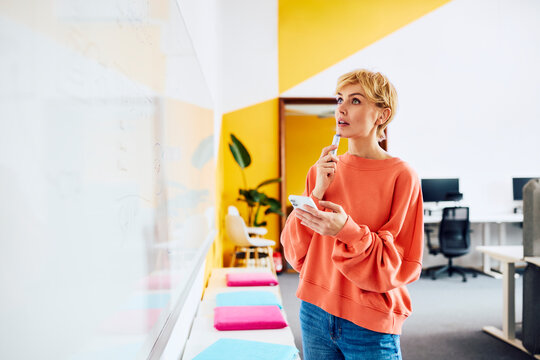Thoughtful businesswoman looks at whiteboard in modern office