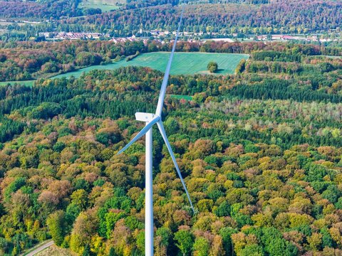 Aerial view of Parc eolien des trois cantons wind turbine surrounded by dense autumn forest and green fields in Etouvans, Bourgogne-Franche-Comte, France.
