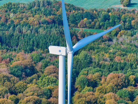 Aerial view of Parc eolien des trois cantons wind turbine surrounded by dense autumn forest with vibrant fall foliage in Etouvans, Bourgogne-Franche-Comte, France.