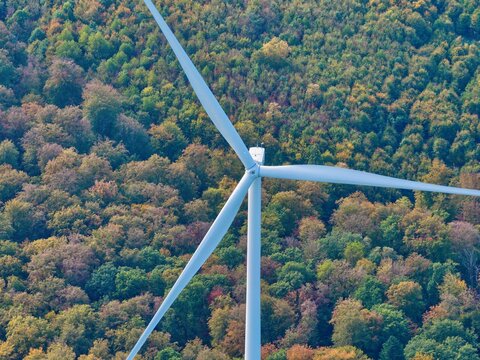 Aerial view of Parc eolien des trois cantons wind turbine rising above a dense forest with vibrant autumn foliage in Etouvans, Bourgogne-Franche-Comte, France.
