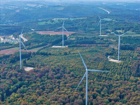 Aerial view of Parc eolien des trois cantons with wind turbines rising above the dense autumn forest in Etouvans, Bourgogne-Franche-Comte, France.